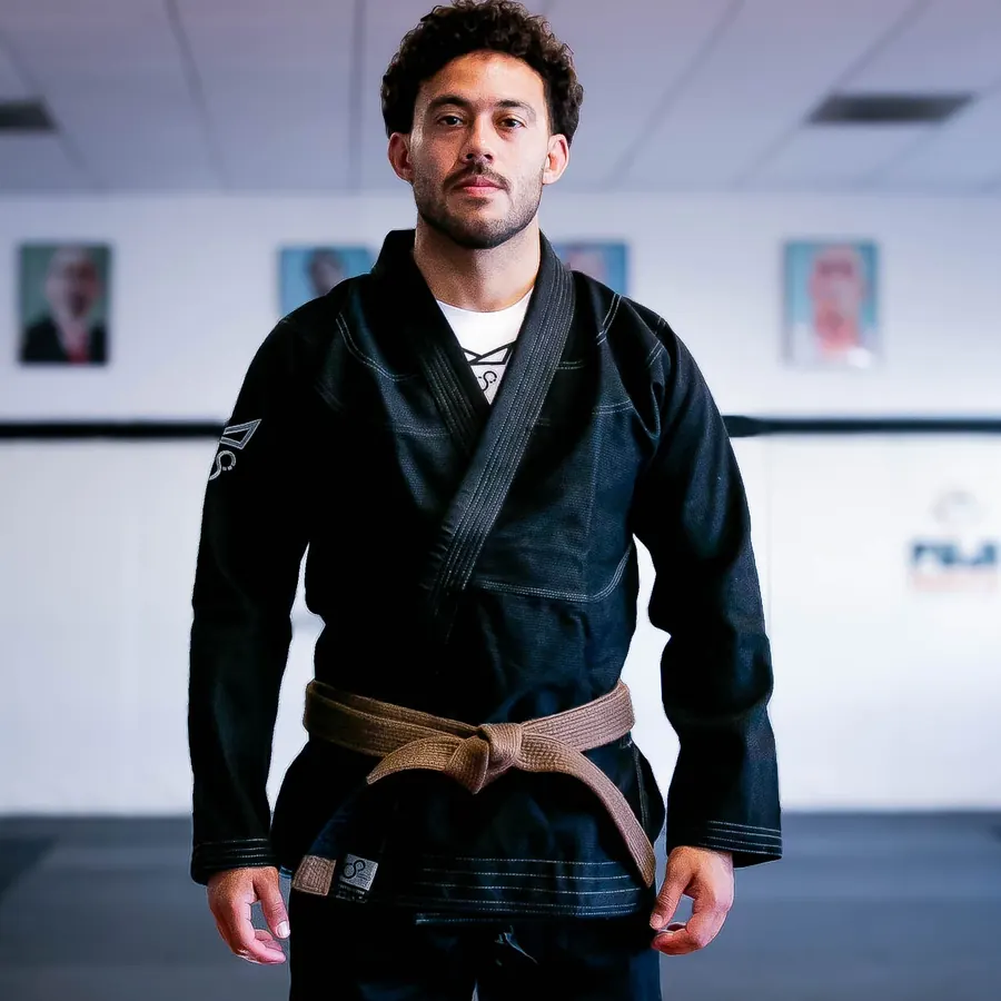 An athlete in the black FNTQ gi and brown belt squares up to you on the mats